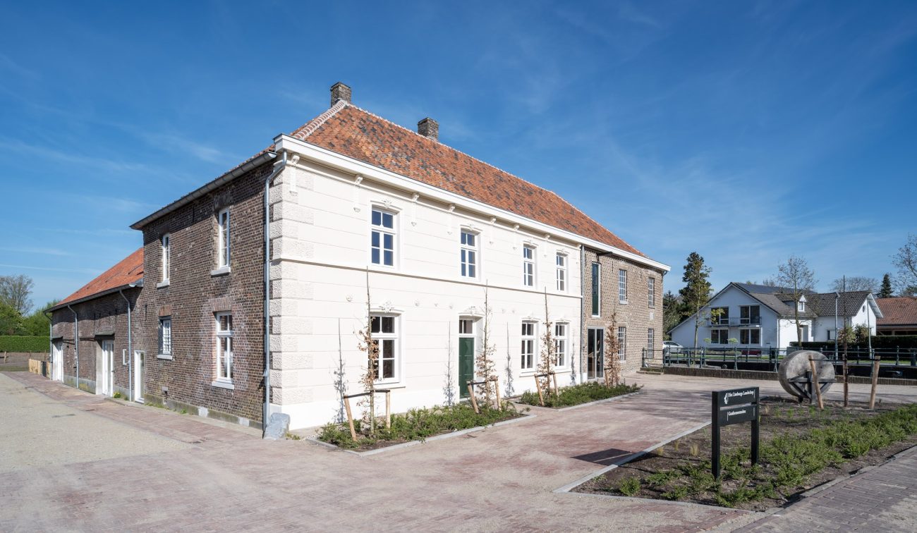 Gerestaureerde Grathemermolen in Grathem – voorgevel met witgepleisterd middendeel, bakstenen zijvleugels en rood pannendak, aan een bestrate binnenplaats met bord en oude molensteen.