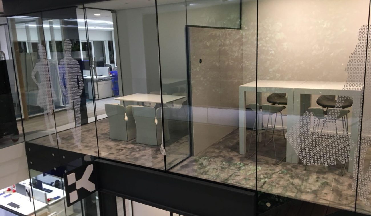Glazen vergaderruimtes aan vide: lage tafel met stoelen, hoge statafel, folie-decor, modern kantoor.