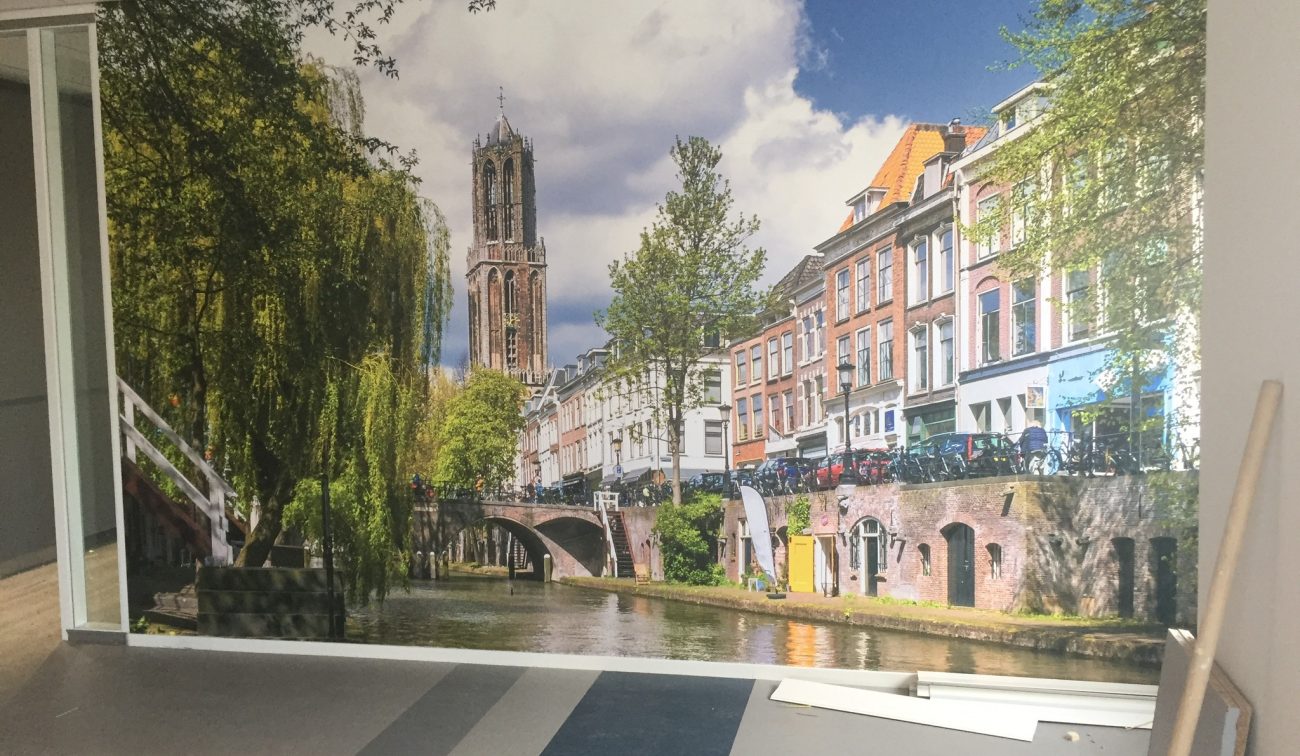 Wandprint Utrecht met Domtoren en Oudegracht: kleurrijke grachtenpanden, brug, bomen, water, kantoor