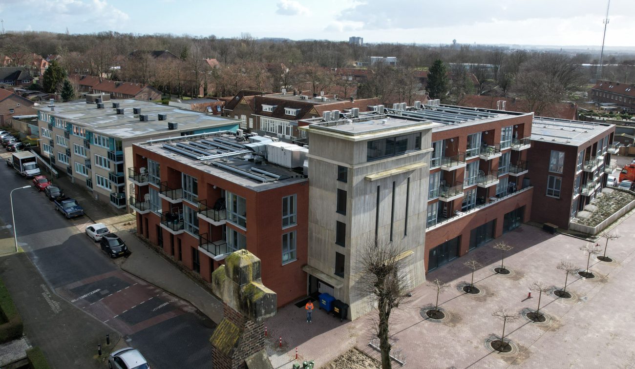 MFA Hart voor Treebeek Brunssum – luchtfoto van bakstenen complex met betonnen toren, balkons en plat dak met installaties aan plein met bomen