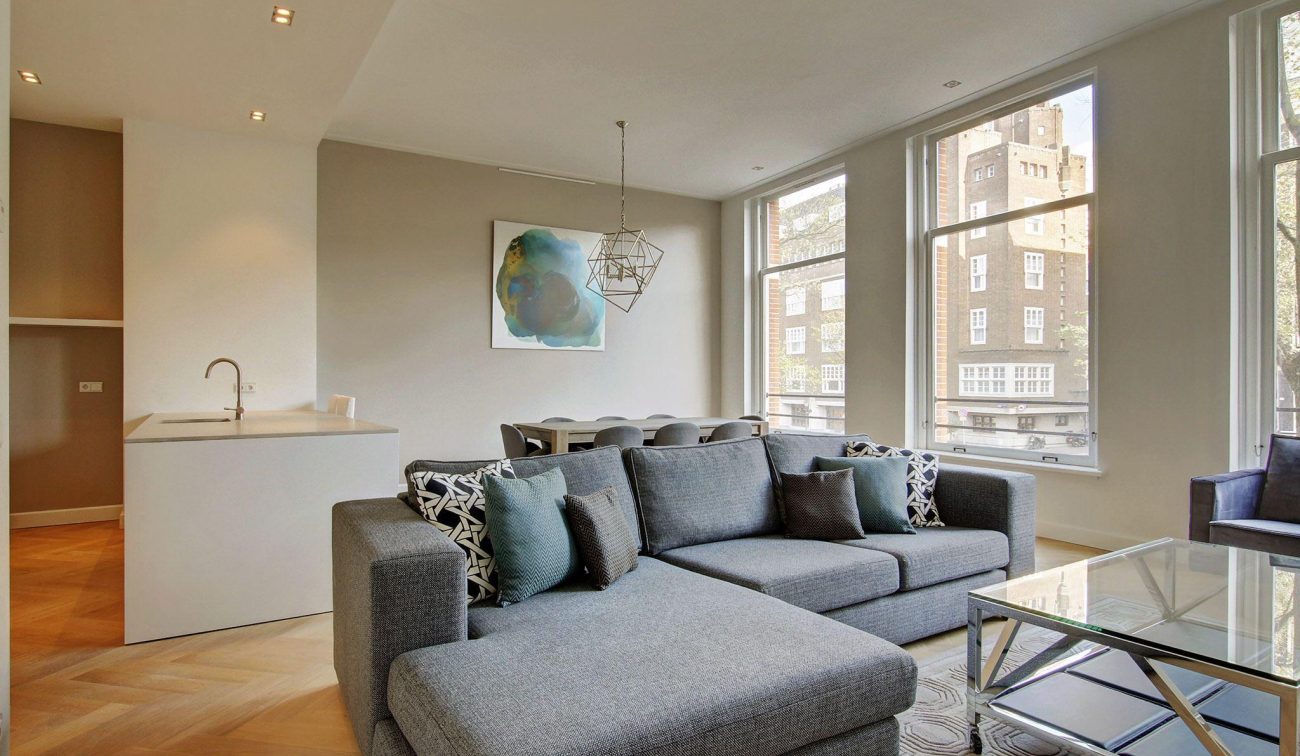 Woonruimte Oudezijds Voorburgwal: hoekbank, glas salontafel, eethoek en veel daglicht