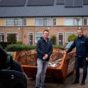 Twee mannen staan voor een afvalcontainer met op de achtergrond een rij woonhuizen met zonnepanelen