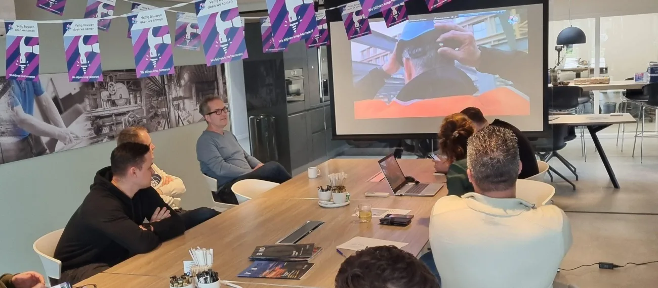 Veiligheidsbijeenkomst met presentatie rond vergadertafel en vlaggenlijn over veilig bouwen