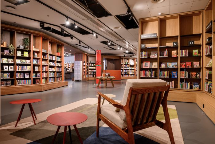 Jeugdboekenafdeling: lage, warme kasten, kleurrijke titels, vloerkleed en comfortabele stoel.