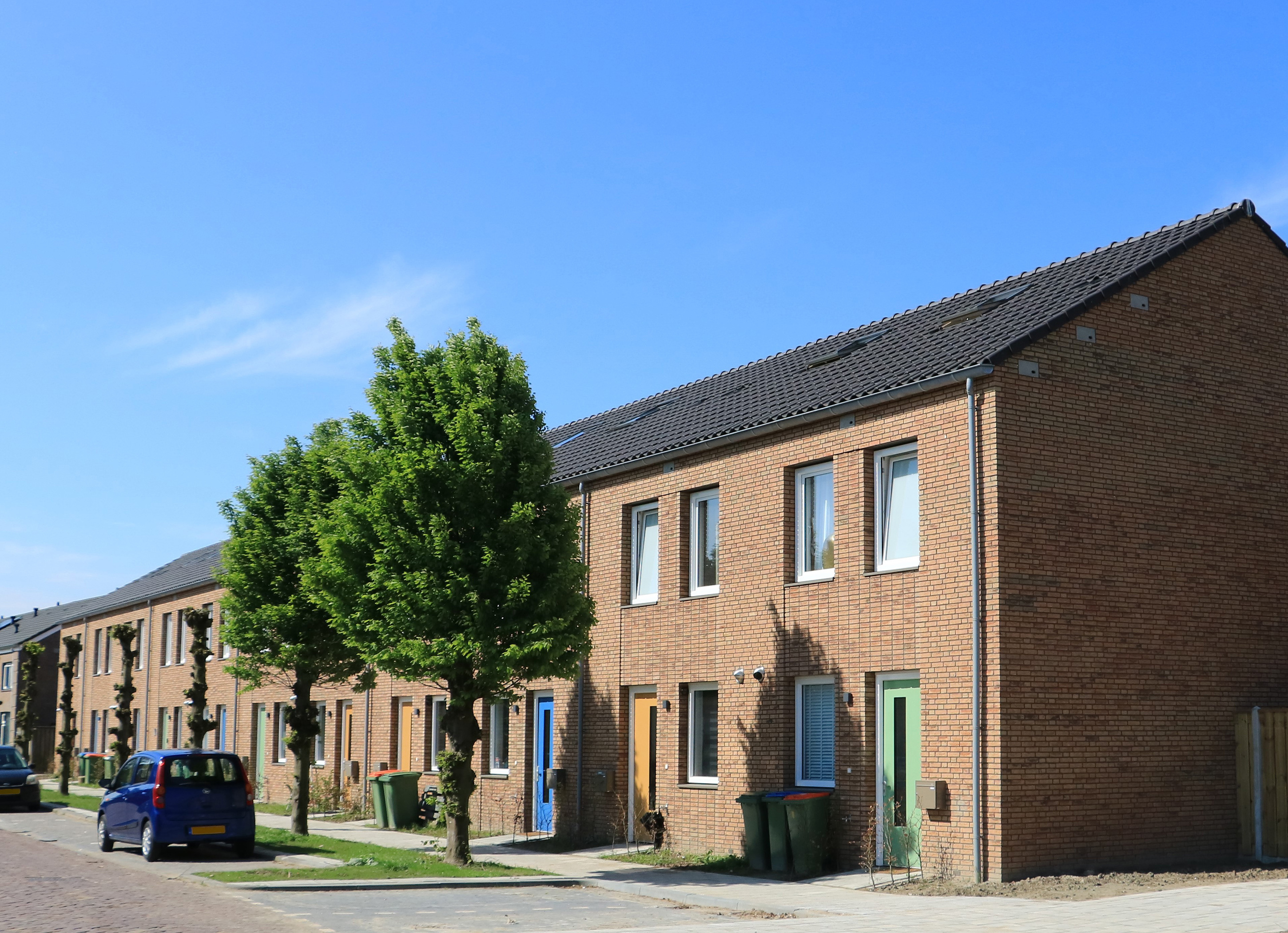 Rijwoningen met bakstenen gevels, gekleurde voordeuren en bomen langs woonstraat