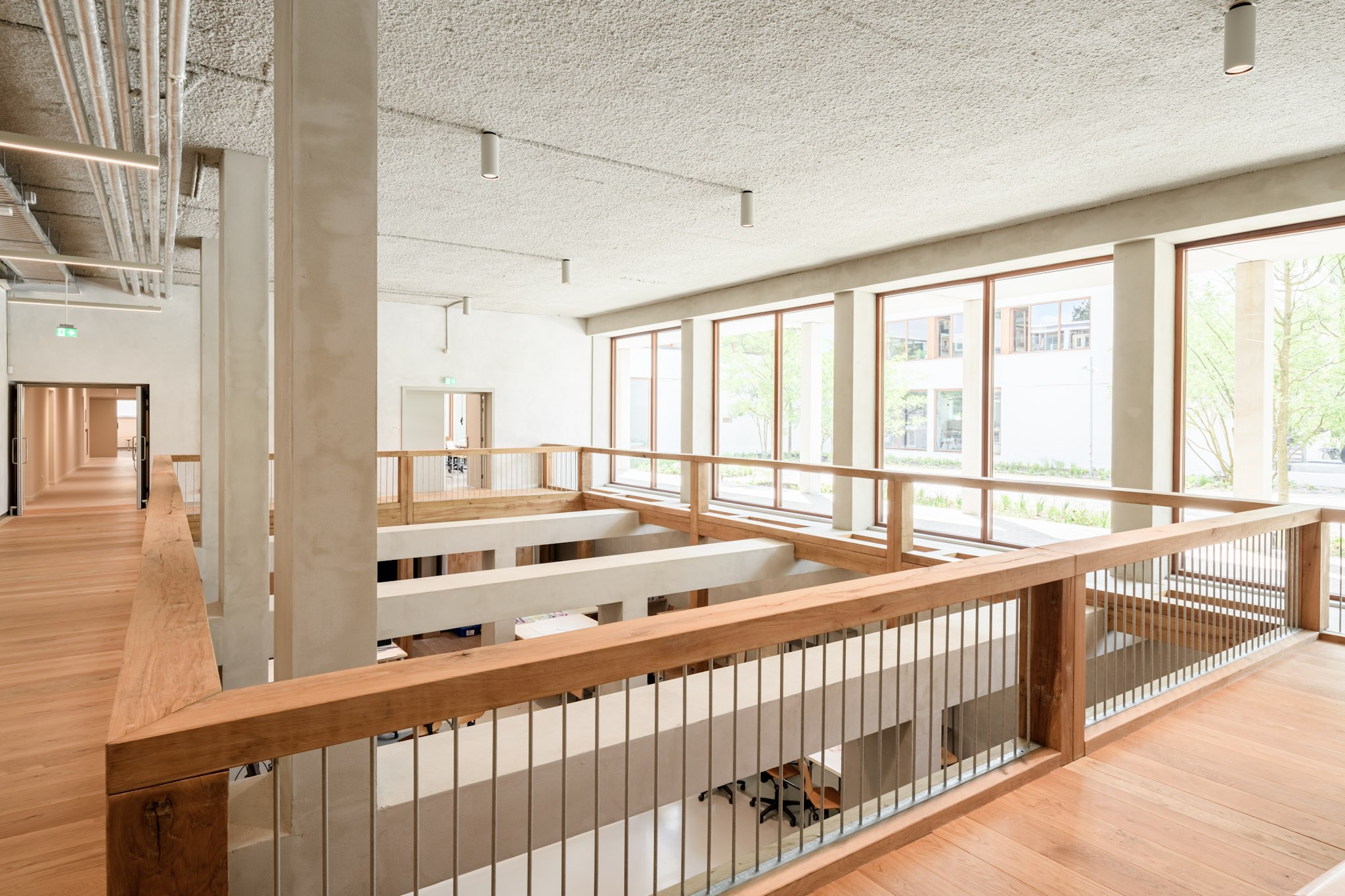 Minimalistisch onderwijsinterieur met zichtbare installaties en akoestisch plafond boven de vide.