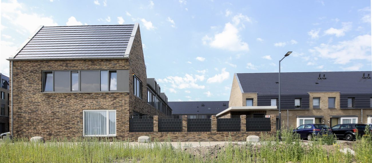 Moderne woningen met bakstenen gevels en schuine daken, gelegen aan straat met voortuinen, grasveld en geparkeerde auto’s in woonwijk