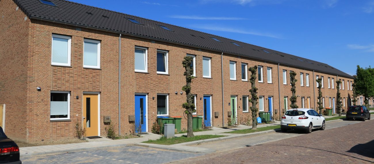 Nieuwbouw conceptwoningen Klundert: rijwoningen in baksteen met gekleurde deuren, bomen en autos.