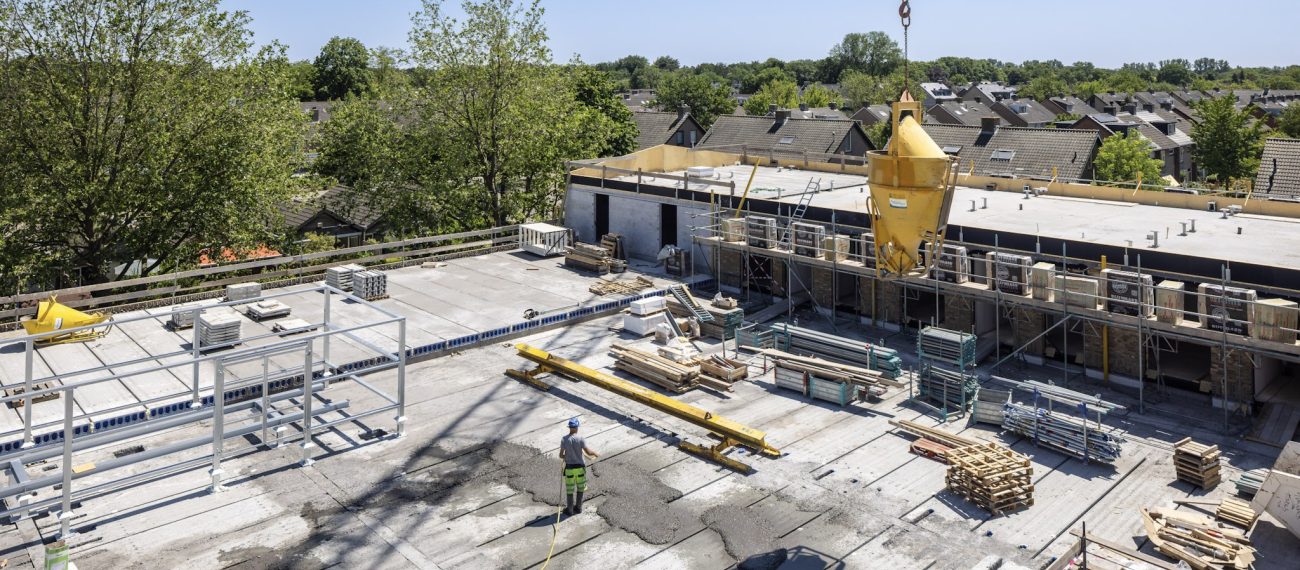 Bouwplaats met werknemers en kraan die materialen plaatsen op het dak van een nieuw wooncomplex.