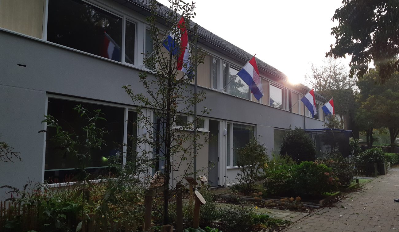 Schuin straatbeeld van de Herculesstraat in Rosmalen waarop de woningen met Nederlandse vlaggen zichtbaar zijn tijdens het groot onderhoudsproject.