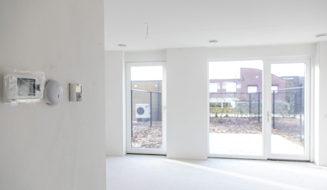 CPO Meerdel Elsloo – lichte woonkamer met witte wanden en kamerhoge tuindeuren naar omheinde tuin met buitenunit warmtepomp