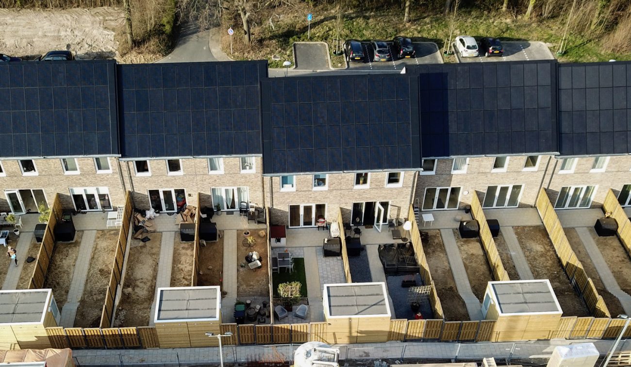 Luchtfoto rij eengezinswoningen in Hulsberg met zwarte zonnepaneeldaken en nieuw aangelegde, omheinde achtertuinen met houten schuttingen en bergingen.