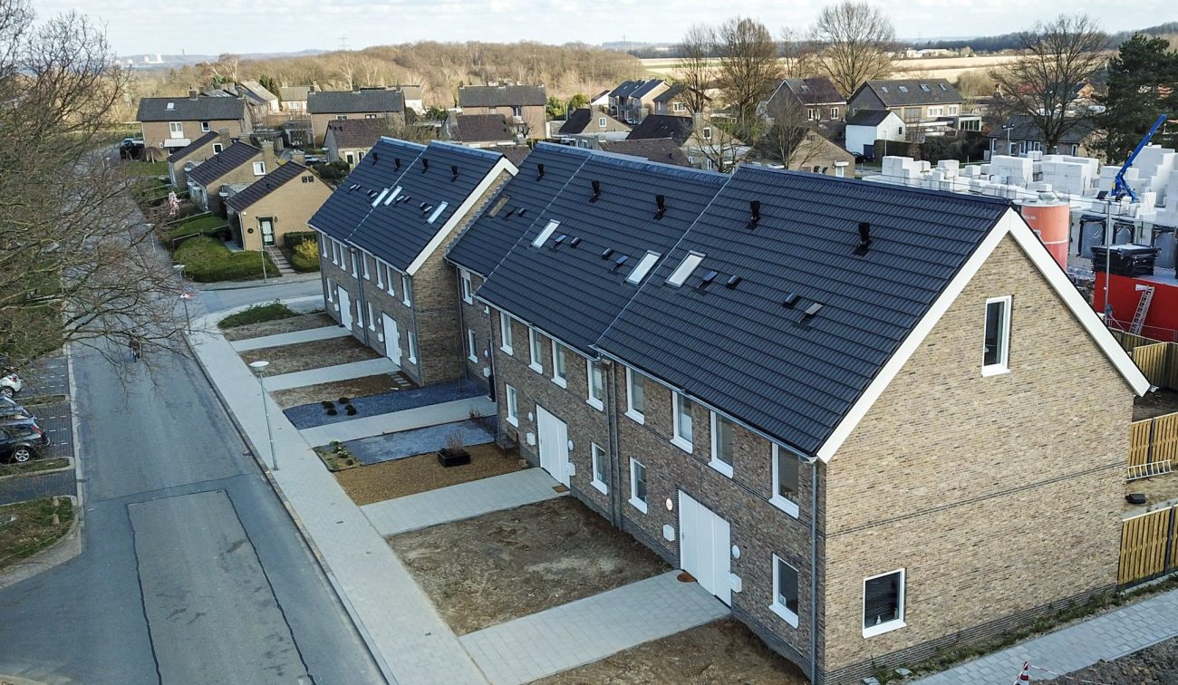 Luchtfoto van nieuwbouw rijwoningen in Hulsberg met bakstenen gevels en donkere zadeldaken met dakramen; nieuwe stoepen en opritten langs een rustige straat.