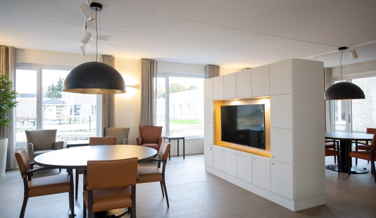 Gezamenlijke woonruimte verpleeghuis Panhuys Hulsberg met ronde tafels en grote hanglampen.