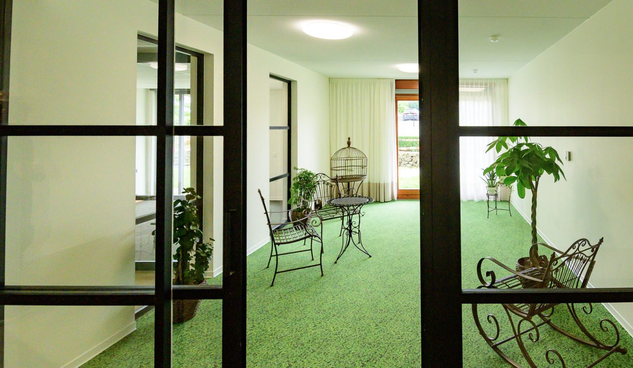 Serre-achtige zitruimte in Hoeve Overhuizen met groen tapijt en smeedijzeren meubels