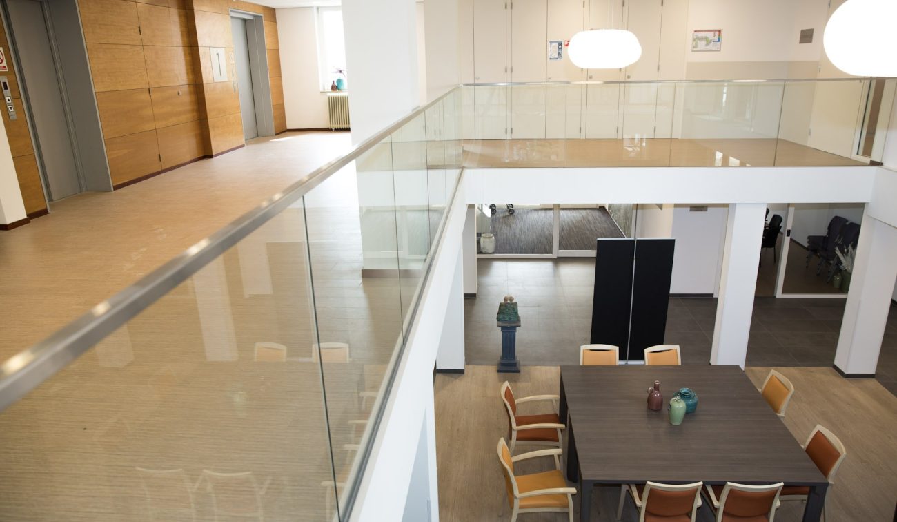 Interieur Beukeloord: open vide met glasbalustrade boven zithoek met tafel en stoelen.