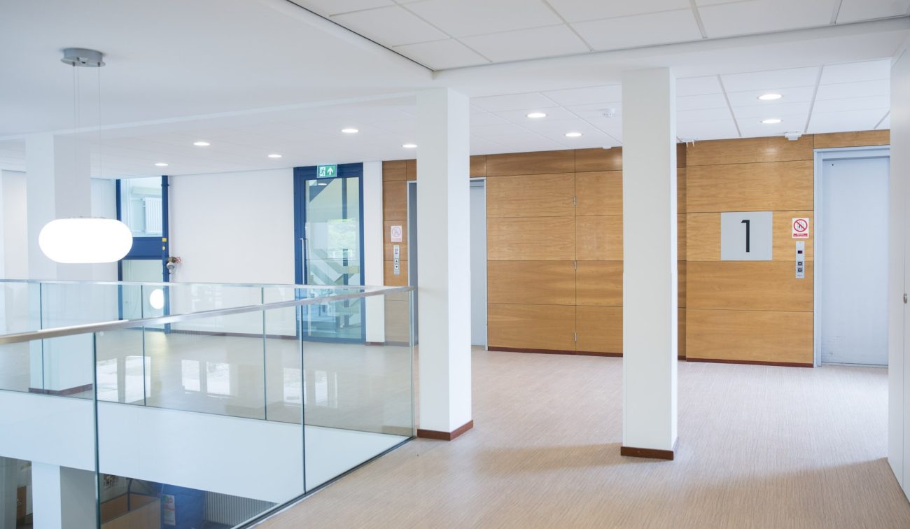 Interieur woonzorgcentrum Beukeloord: open vide met glasbalustrade en houten liftlobby.