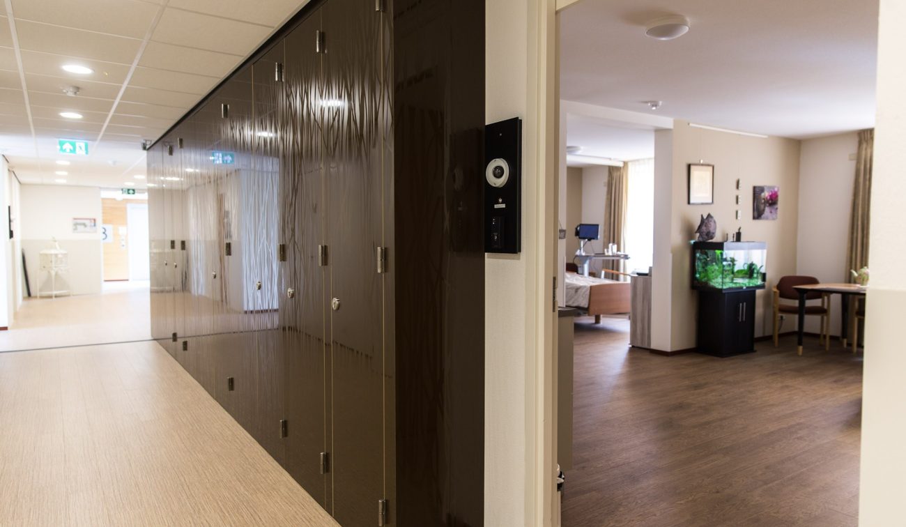 Gang woonzorgcentrum Beukeloord met glanzende kastenwand en doorkijk naar zorgkamer met aquarium.