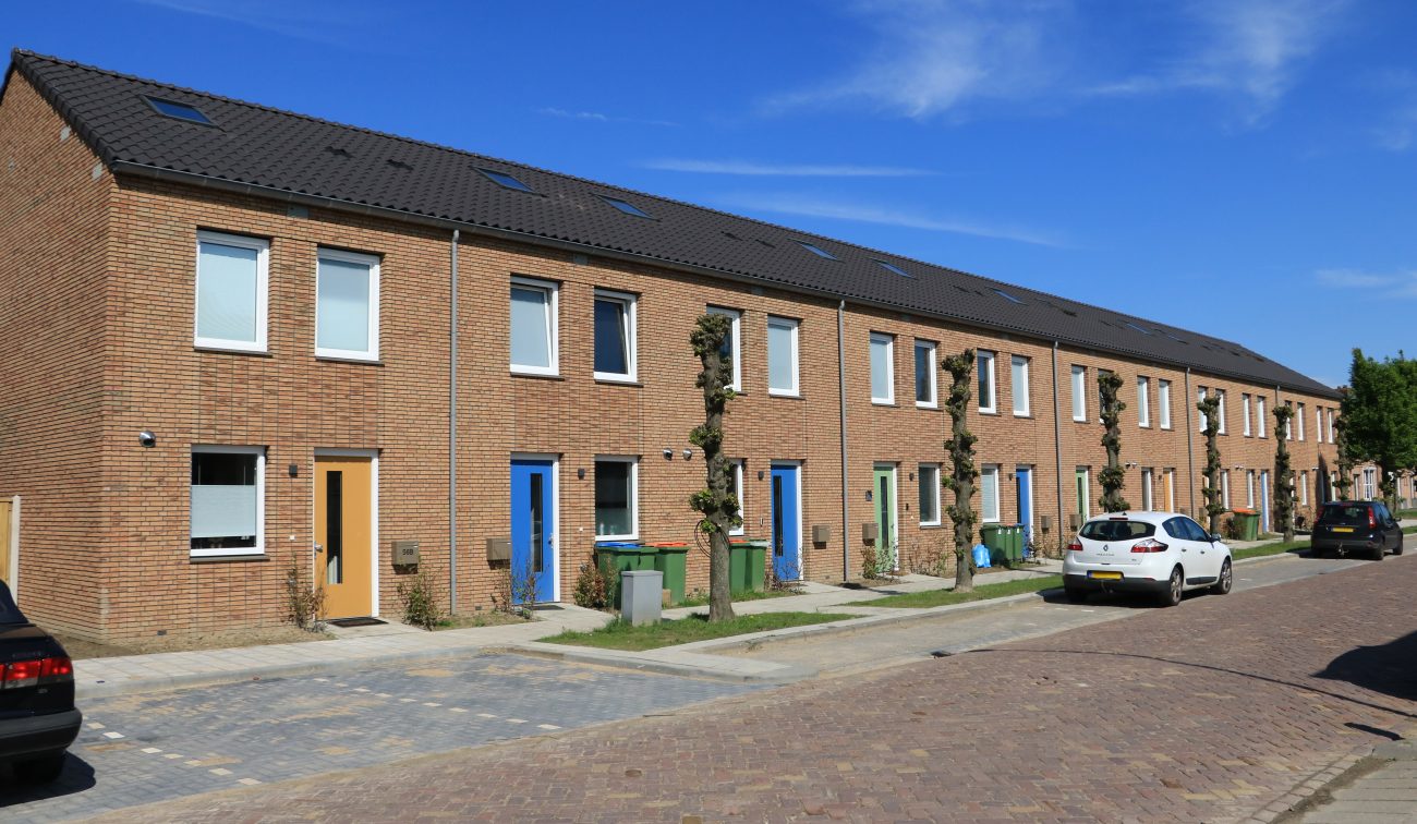 Nieuwbouw conceptwoningen Klundert: rijwoningen in baksteen met gekleurde deuren, bomen en autos.