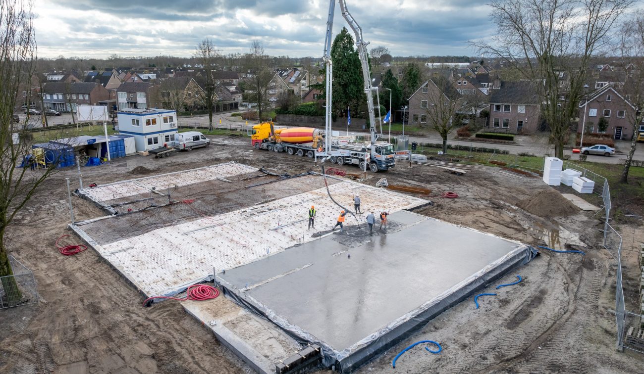 Antoniusschool Zundert: storten beganegrondvloer met betonpomp, mixerwagens vaklieden op bouwplaats.