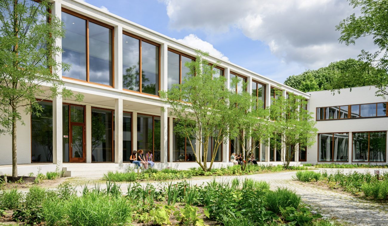 Transparante onderwijsgevel met veranda langs de patio; leerlingen relaxen tussen het groen.