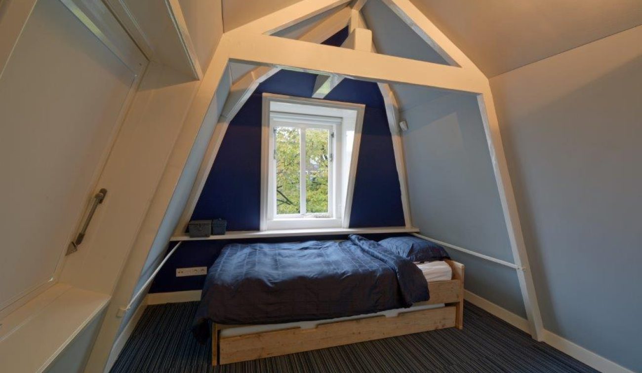 Renovatie Egelantiersgracht: compacte slaapkamer onder kap, zichtbare spanten en blauwgrijze wanden
