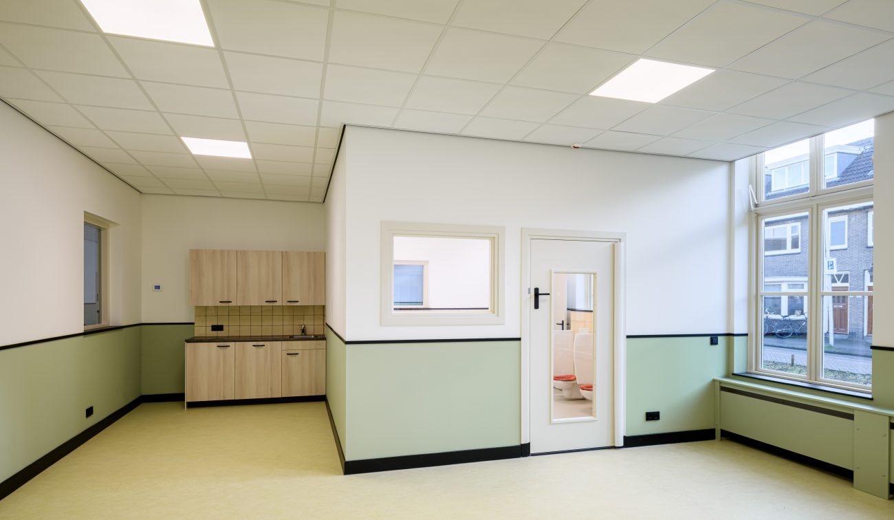 Hoeklokaal met groot kozijn, interne deur met kijkruit en nette afwerking in groen-wit.