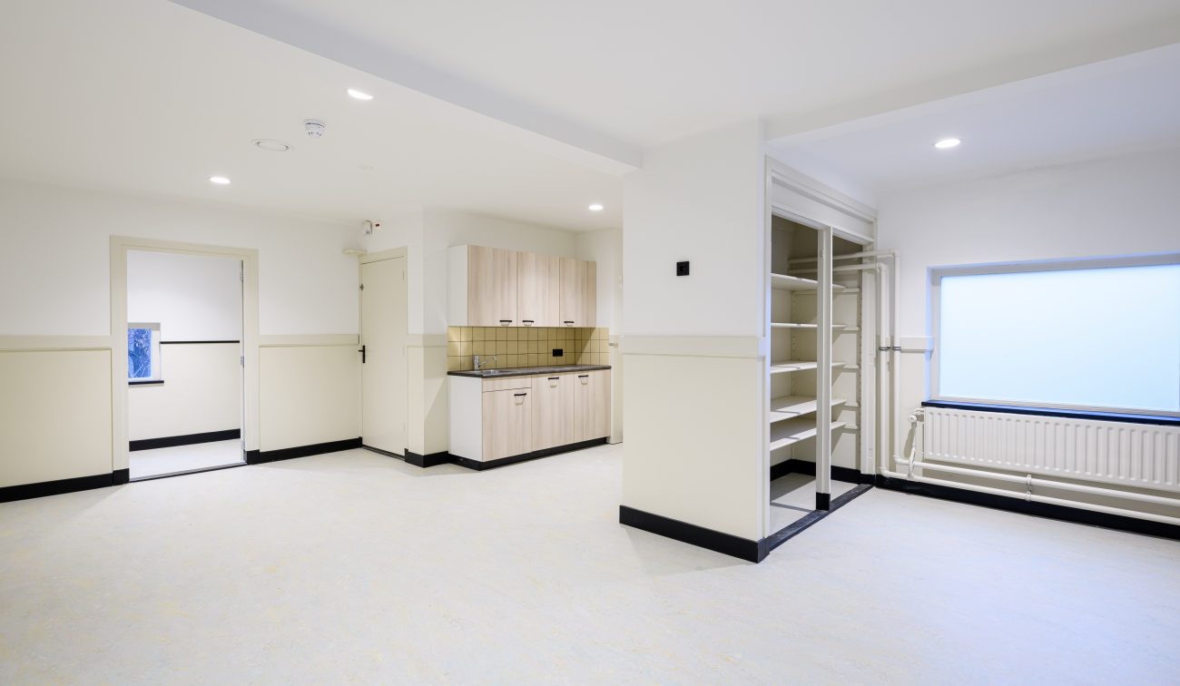 Opgeknapte lesruimte met kitchenette, ingebouwde open kasten en matglasraam met radiator.