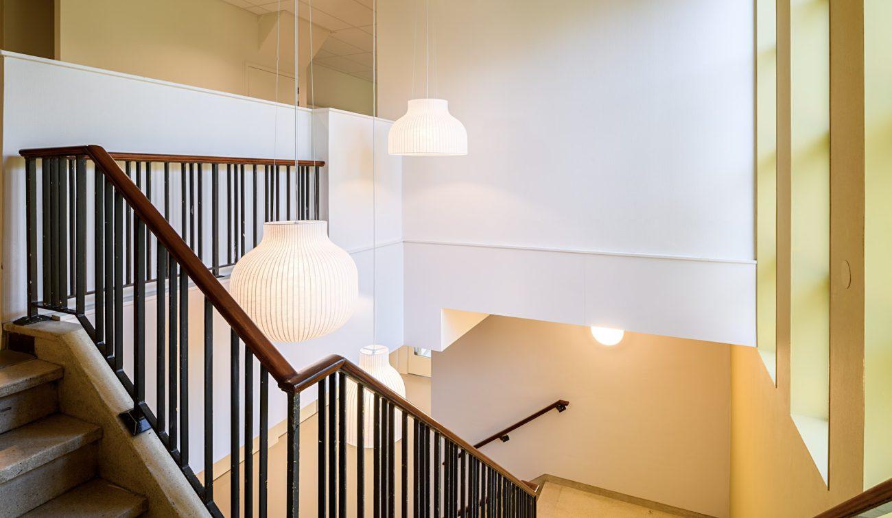 Schooltrap OBS De Fakkel: licht trappenhuis met houten leuning, zwarte spijlen en ronde pendels
