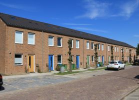 Nieuwbouw conceptwoningen Klundert: rijwoningen in baksteen met gekleurde deuren, bomen en autos.