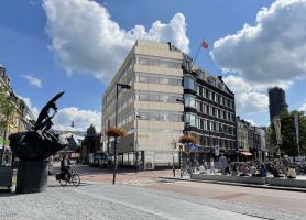 Gevel van een kantoorpand midden in een stad met blauwe lucht en bewolking