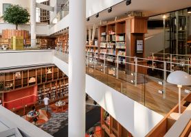 Lichte atriumbibliotheek met houten boekenkasten, glazen balustrades en witte kolommen.