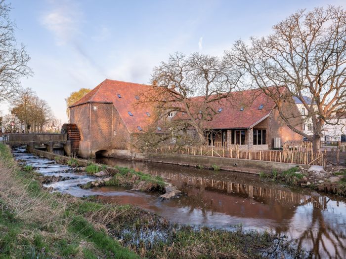Grathemermolen in Grathem – gerestaureerde watermolen met rood pannendak en waterrad aan de beek, omringd door bomen en een houten hekwerk.