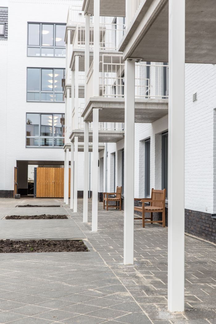 Hof te Berkel Horst – witgemetselde galerij met slanke kolommen en uitkragende balkons, houten banken en plantvakken in aanleg