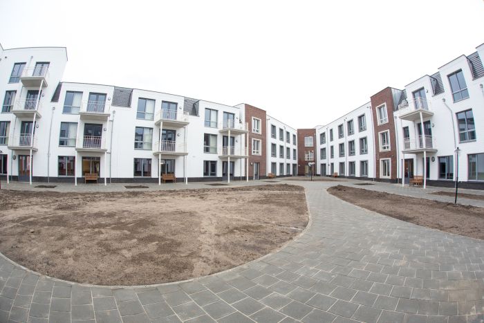 Hof te Berkel Horst – U-vormige binnentuin met slingerpad, zandvakken in aanleg en witte/rode appartementengevels met balkons