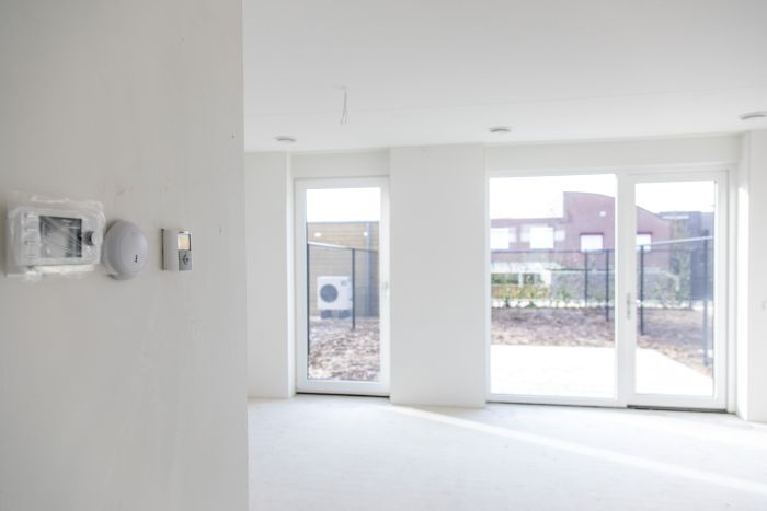 CPO Meerdel Elsloo – lichte woonkamer met witte wanden en kamerhoge tuindeuren naar omheinde tuin met buitenunit warmtepomp