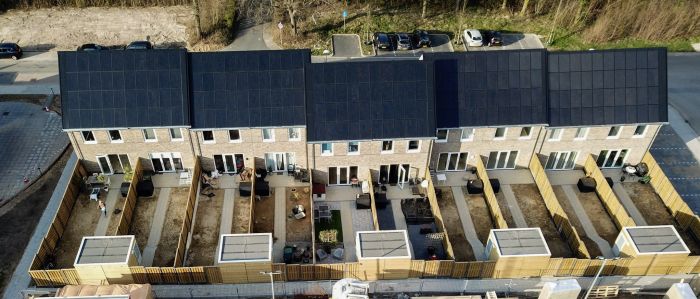 Luchtfoto rij eengezinswoningen in Hulsberg met zwarte zonnepaneeldaken en nieuw aangelegde, omheinde achtertuinen met houten schuttingen en bergingen.