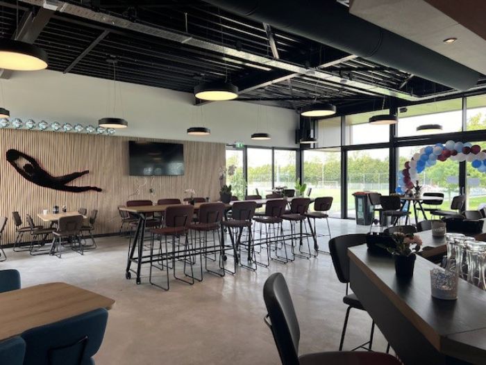 Clubkantine FC Landgraaf: hoge tafels, hanglampen, lamellenwand met tv en glas naar de velden