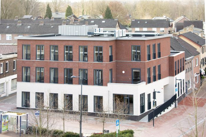 Nieuwbouw zorgcomplex Cicero Bleekstaete in Schinveld: modern hoekgebouw van drie verdiepingen met rood bakstenen gevel en witte plint, veel hoge ramen en een plat dak met installaties; gelegen aan een straat met jonge, bladloze bomen en een bushalte, omringd door woonhuizen.