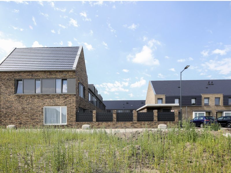 Nieuwbouwwijk met moderne bakstenen woningen en donkere dakpannen op een zonnige dag in woongebied.